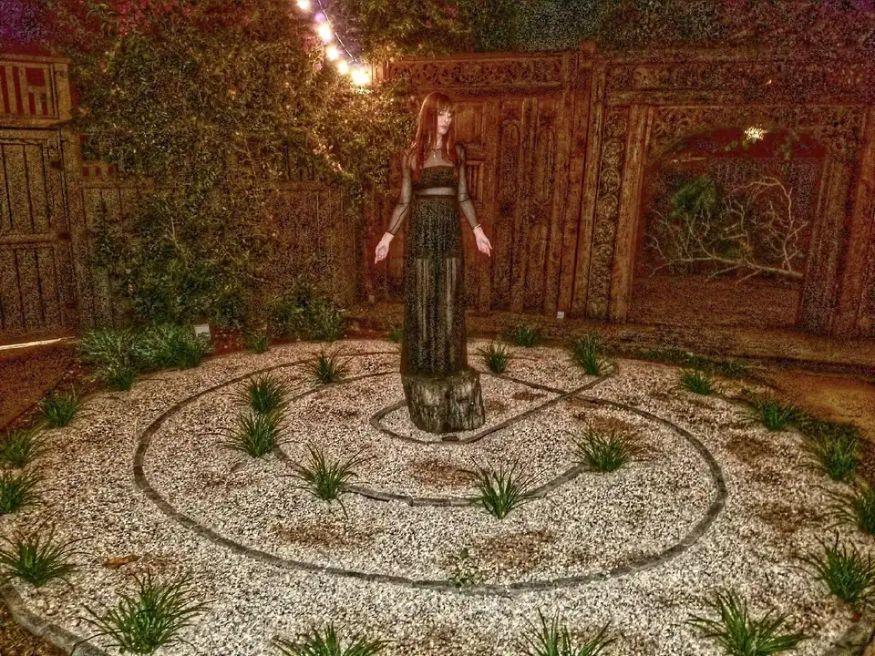 A three-circuit stone labyrinth surrounding a standing sculpture beneath garden lights.